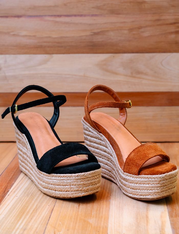 Pair of fashionable wedge sandals with rope espadrille soles displayed indoors on wooden flooring.