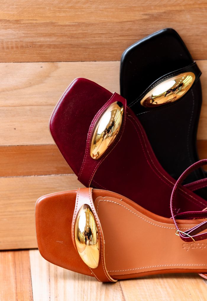 Stylish women's sandals with gold oval decorations stacked on a wooden background for a chic look.