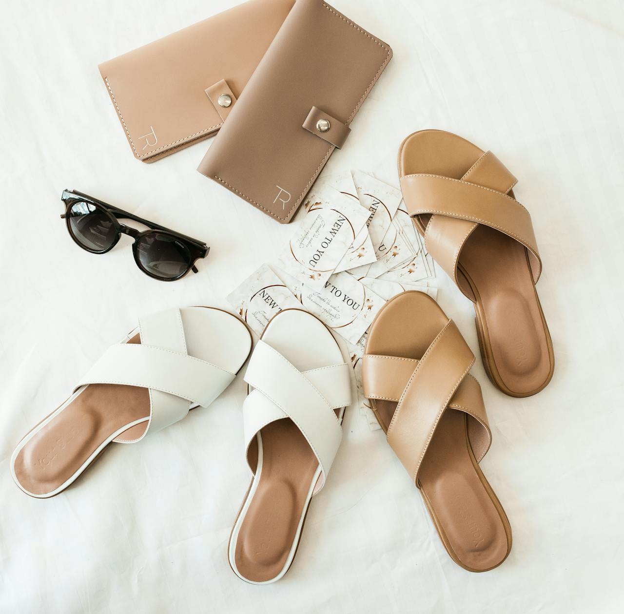 Elegant flat lay of summer footwear, wallets, and sunglasses on a white background.